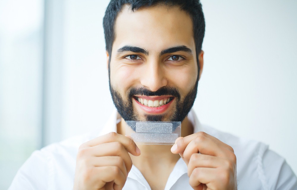 Smiling man holding whitening strip.